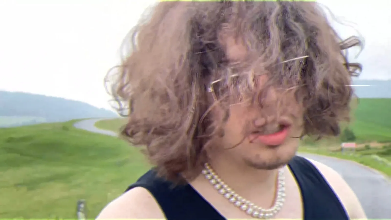 Close-up of Srrlovych in sunglasses and a pearl necklace, hills behind