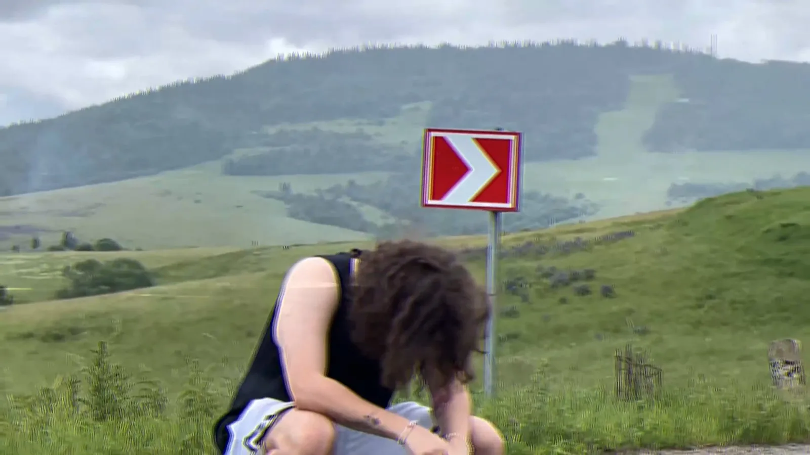 Srrlovych crouches on a mountain road next to a red chevron sign